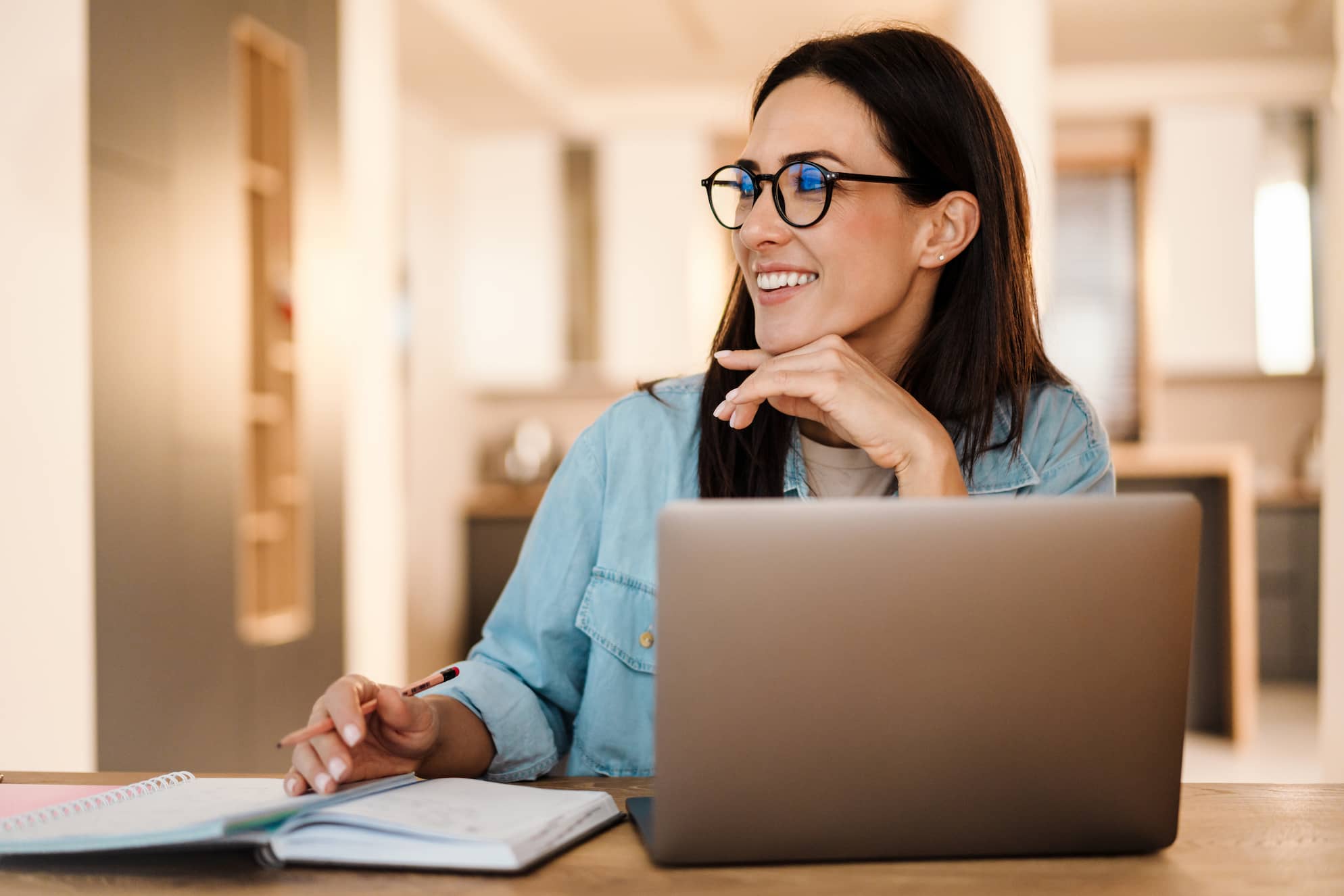 Happy woman writing down notes while working with laptop
