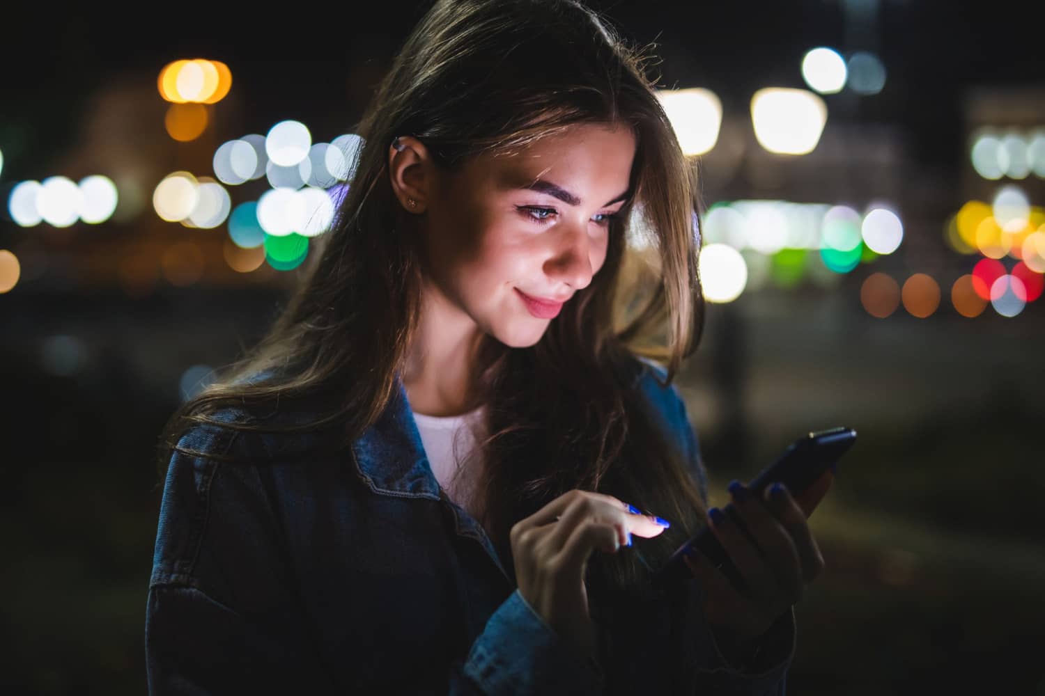 A girl using a smartphone at night in the street with beautiful lights.